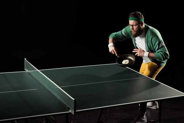 tennis player with frying pan with egg playing table tennis isolated on black