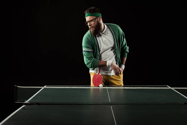 bearded tennis player leaning on racket on tennis table isolated on black