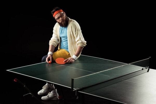 thoughtful tennis player sitting on tennis table isolated on black