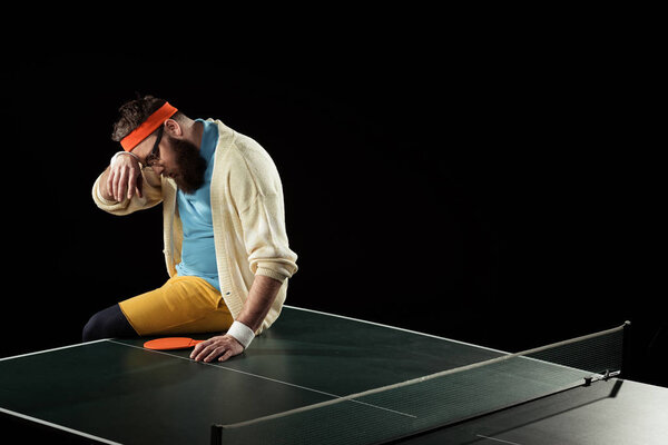 tired tennis player sitting on tennis table isolated on black