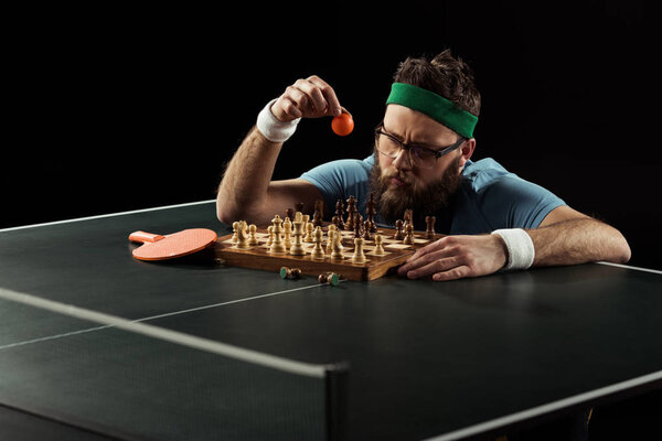bearded sportsman throwing tennis ball on chess board on tennis table isolated on black