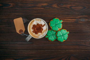 top view of cup of coffee with blank label and cookies in shape of clovers on wooden table clipart