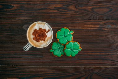 top view of cappuccino and cookies in shape of shamrocks on wooden table clipart