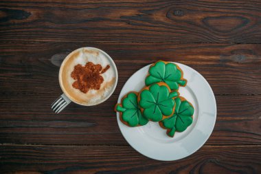 top view of tasty cappuccino and cookies in shape of clovers on wooden table clipart