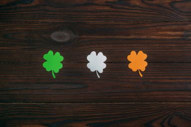 top view of three clovers in colors of irish flag on wooden table clipart