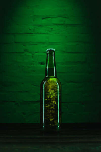 close-up view of single green glass bottle of fresh cold beer in green light