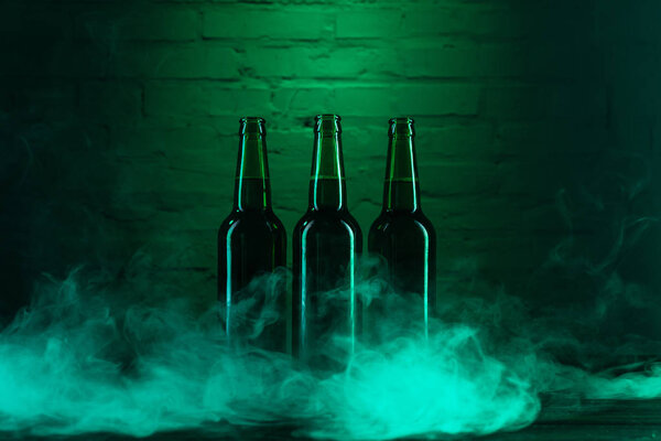 three green beer bottles and smoke near green brick wall