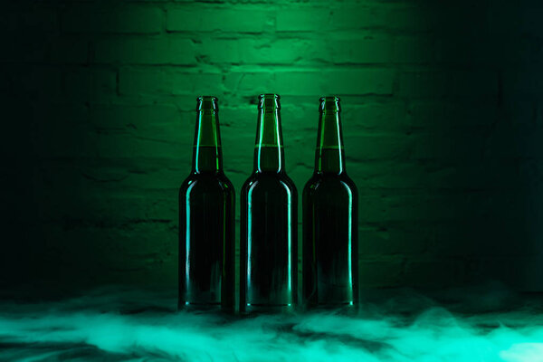 three open green beer bottles and smoke in green light 