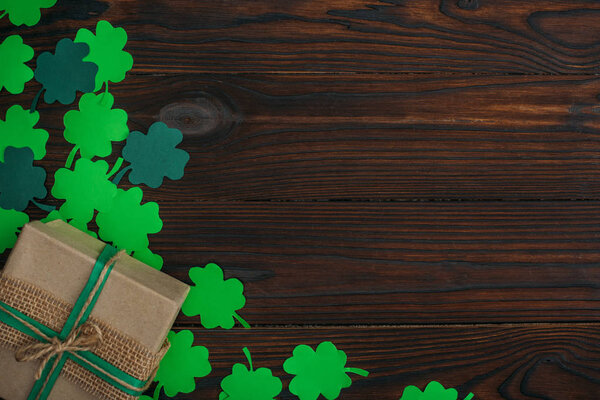 top view of wrapped gift box and green shamrocks on wooden table