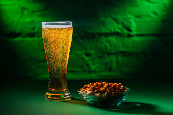 close-up view of glass with fresh cold beer and salted peanuts on plate