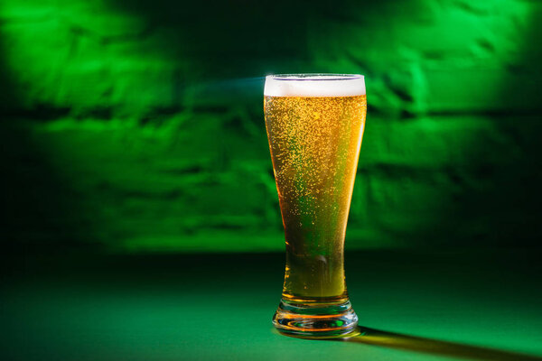 close-up view of glass with fresh cold beer in green light 