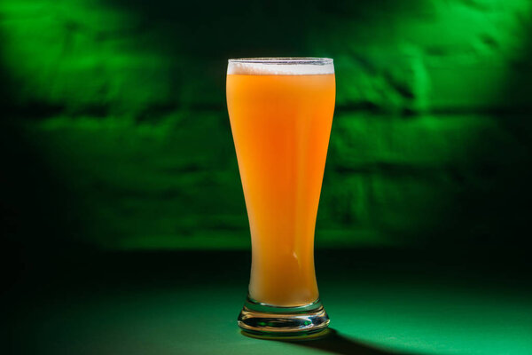 close-up view of glass with fresh cold amber beer in green light 