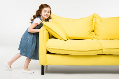 Stylish little kid in dress pushing sofa isolated on white
