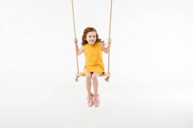 Little stylish child in dress riding on swing isolated on white clipart