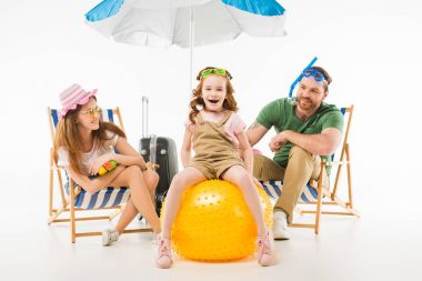 Happy little kid in swimming goggles sitting on ball between mother and father isolated on white, travel concept clipart