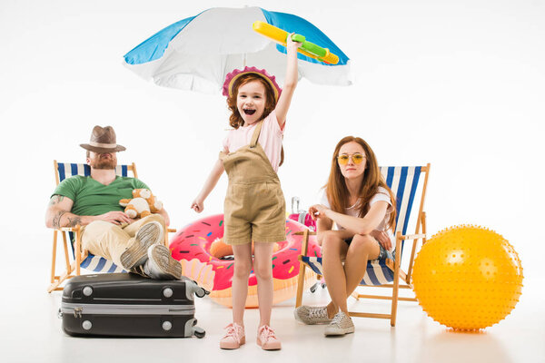 Father sleeping in sun loungers while daughter standing with water gun near mother isolated on white, travel concept