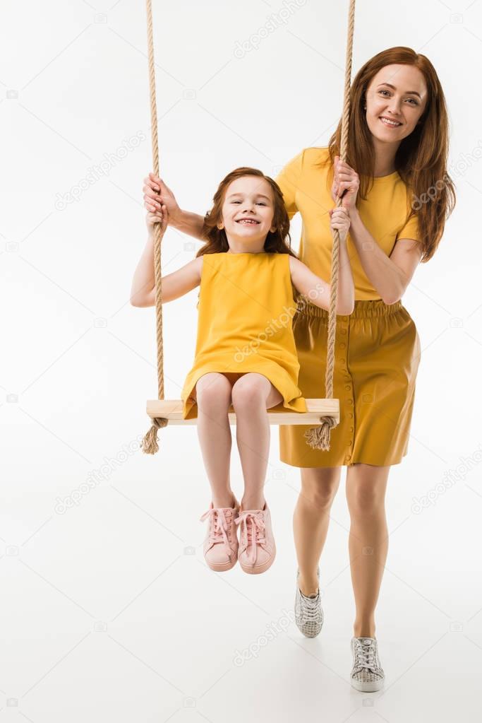 Mother riding happy little daughter on swing isolated on white