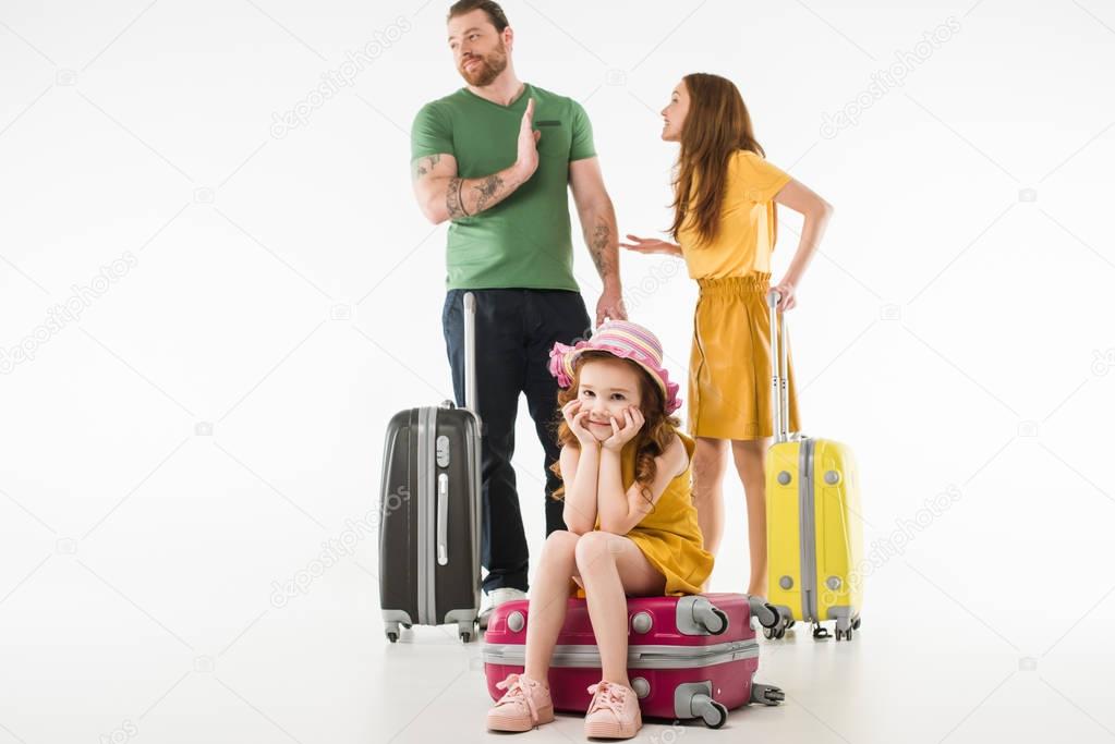 Upset little child sitting on suitcase while parents arguing isolated on white, travel concept