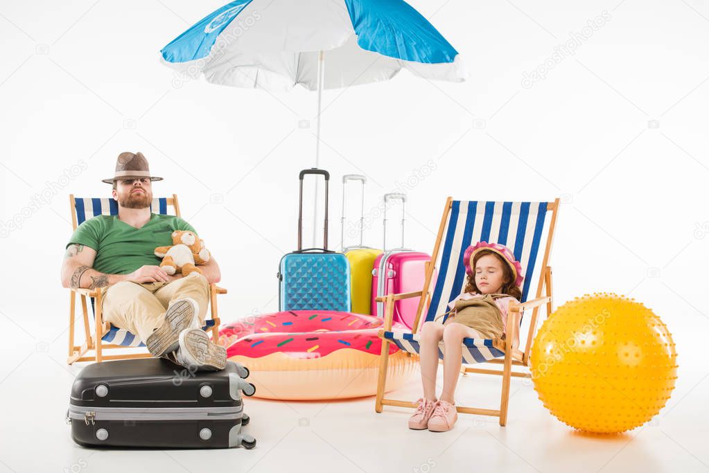 Father and daughter in hats sleeping in sun loungers isolated on white, travel concept