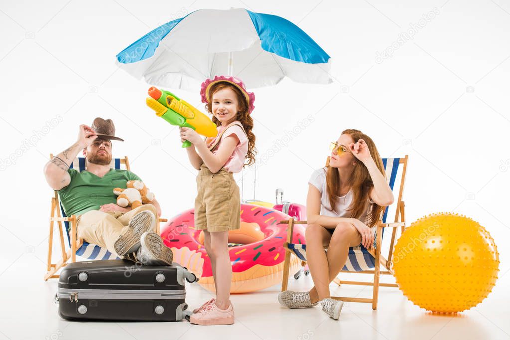 Family of tourists with sun loungers, sunshade, flotation ring and water gun isolated on white