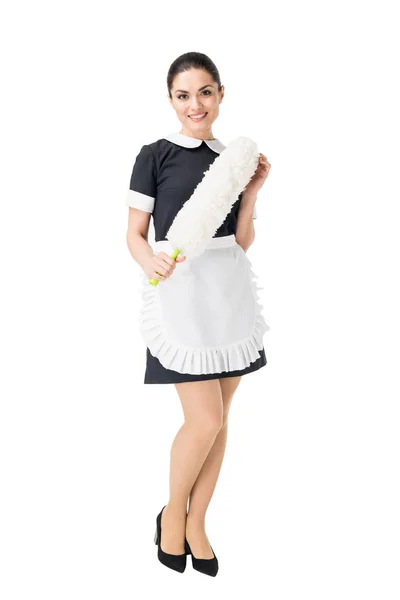 Young maid in professional uniform holding duster isolated on white