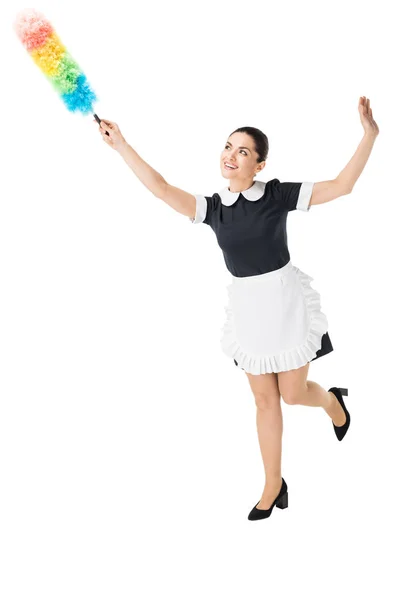 Young maid in professional uniform using colorful duster isolated on white