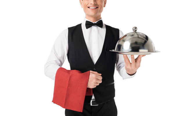 Smiling professional waiter presenting serving tray with cover isolated on white