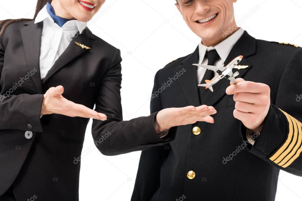 Smiling stewardess and pilot holding toy plane isolated on white