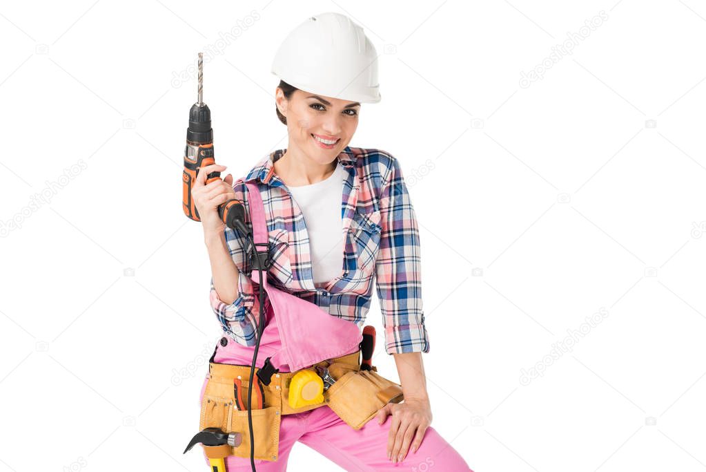 Smiling woman builder in overalls holding drill isolated on white