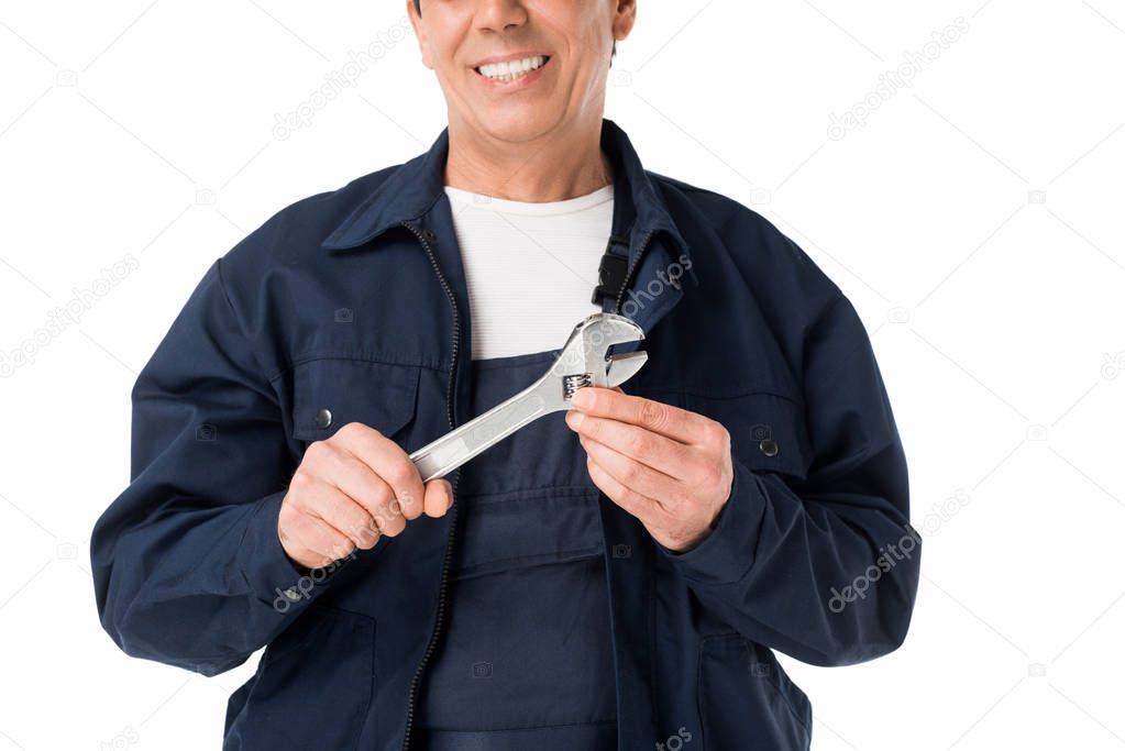 Cheerful plumber in uniform holding adjustable wrench isolated on white