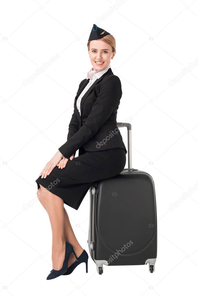 Young female stewardess sitting on suitcase isolated on white