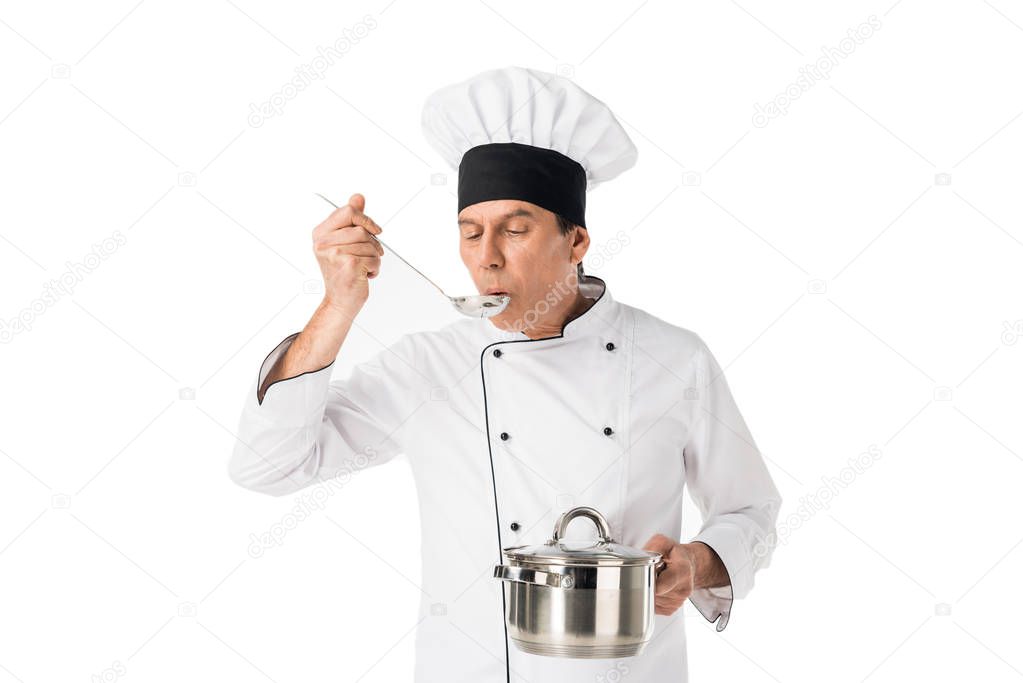Man in chef uniform holding pan and tasting food isolated on white