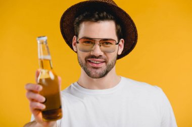 yakışıklı genç adam şapka ve yaz içki şişesiyle tutarak ve sarı izole kamera gülümseyen güneş gözlüğü 