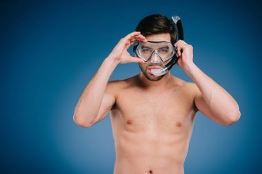 handsome shirtless young man in snorkel and scuba mask looking at camera on blue  clipart
