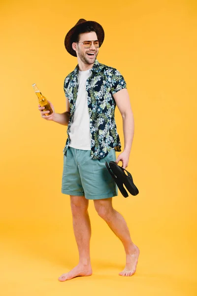 微笑的年轻赤脚男子在短裤持有夏季饮料瓶和触发器隔离黄色 — 图库照片