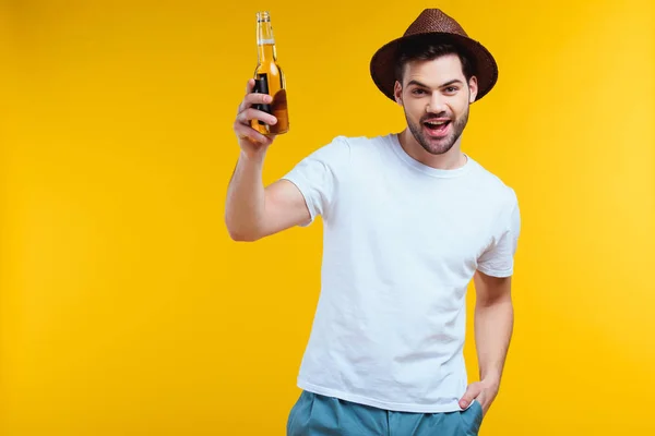 开朗的年轻人在帽子举行的夏天饮料瓶和微笑着在黄色的相机隔离 — 图库照片
