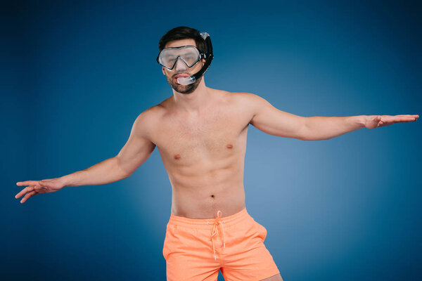 handsome shirtless young man in shorts wearing snorkel and diving mask on blue