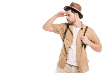 young traveler in hat holding backpack and looking away isolated on white clipart
