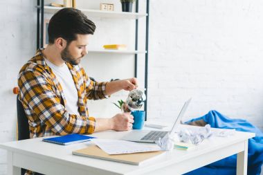 Genç adam kahve Kupası ev ofis laptop ile tabloda dökme
