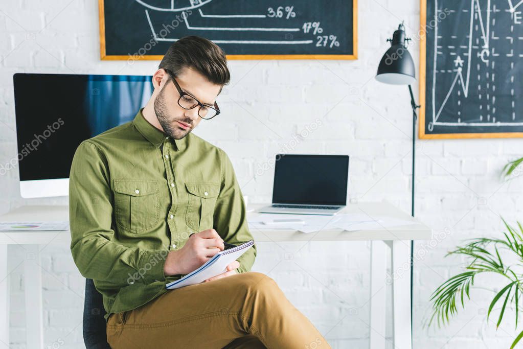 Thoughtful businessman taking notes by working table in light office