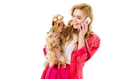 Pembe elbise telefon ve holding sevimli köpek üzerinde beyaz izole konuşurken sarışın kadın