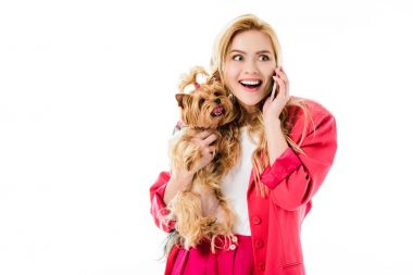 Pembe ceket holding Yorkshire terrier ve üzerinde beyaz izole telefonda konuşurken giyen genç kız