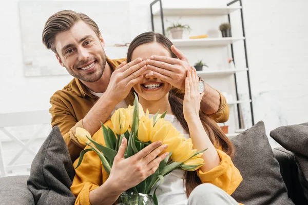快乐的年轻人覆盖着女友的眼睛 并呈现她的花束 — 图库照片