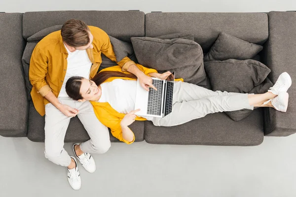 女性は彼氏の膝の上に横たわると自宅の居心地の良いソファでノート パソコンを操作のトップ ビュー — ストック写真