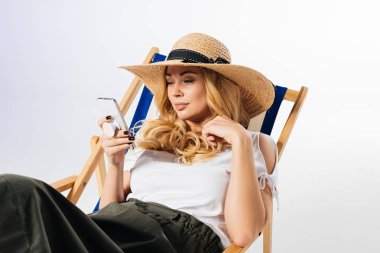 Smiling woman with smartphone resting in deck chair on white background