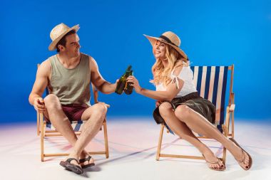 Man and woman drinking beer resting in deck chairs on blue background clipart