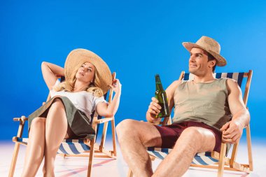Woman sitting in lounge chair by man with beer on blue background clipart