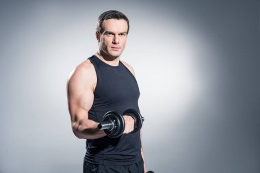 Sportsman working out with heavy dumbbells on grey background clipart