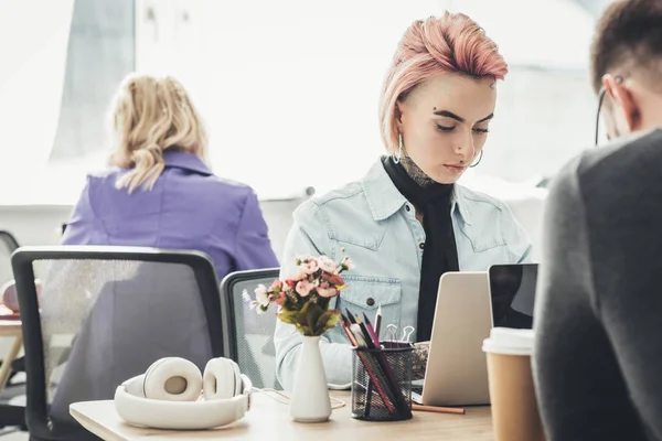 selective focus of tattooed businesswoman at workplace with colleagues near by in office