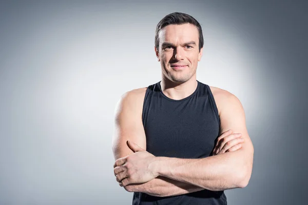 Sportsman standing with folded arms on grey background